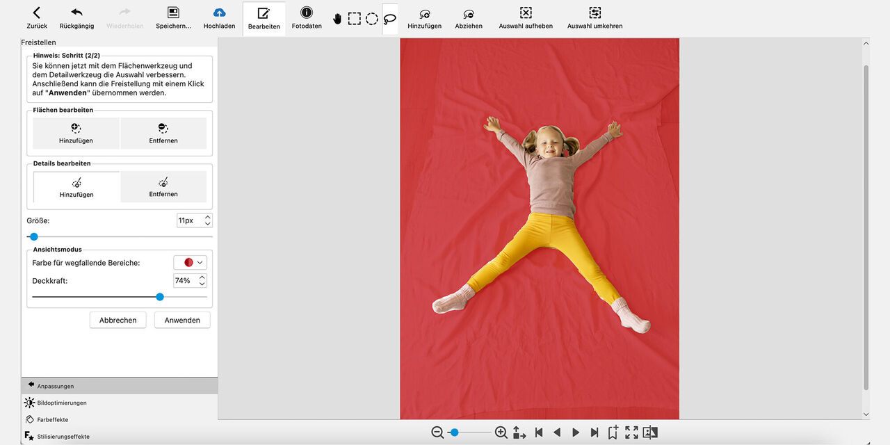 Snímka obrazovky z programu CEWE fotosvet: Dievča leží na zemi na rozprestretej deke a usmieva sa do kamery. Má natiahnuté obe ruky a nohy ďaleko od seba. Pozadie, na ktorom dievča leží, je sfarbené na červeno.